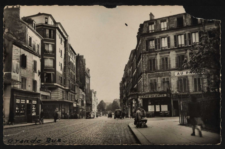 17 - Boulogne-Billancourt, rue J-B Clément, Boulogne-Billancourt . avenue Jean-Baptiste Clément . - perspectiveAu premier plan, à gauche, une confiserie (au dessus une publicité pour Petit Lu) et une charcuterie puis la rue d'Aguesseau.A droite, la rue de l'Eglise et le café des Arts. Au centre, des voitures.