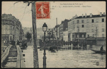 Les Inondations de Paris 1910 - 14 - Boulogne-sur-Seine - Rond-Point, Boulogne-Billancourt . rond-point Rhin-et-Danube . - Crue de la Seine, janvier 1910 - Vue sur le rond-point Rhin-et-Danube inondé. Au premier plan, à gauche, des passerelles de fortune. A droite, un monsieur à bord d'une embarcation de secours. Au second plan, un groupe de personne.