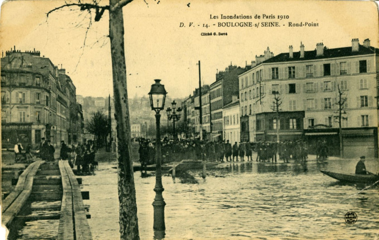 Les Inondations de Paris 1910 - 14 - Boulogne-sur-Seine - Rond-Point, Boulogne-Billancourt . rond-point Rhin-et-Danube . - Crue de la Seine, janvier 1910Vue sur le rond-point Rhin-et-Danube inondé. Au premier plan, à gauche, des passerelles de fortune. A droite, un monsieur à bord d'une embarcation de secours. Au second plan, un groupe de personne.